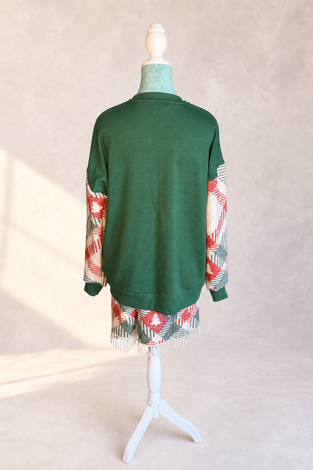 Back view of The Noel Rework showing the forest green sweatshirt body, woven textile sleeves, and fringed lower panel
